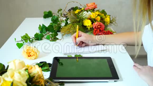 使用平板电脑的花艺设计师女孩的特写将花编成程序并将m写成便条视频的预览图