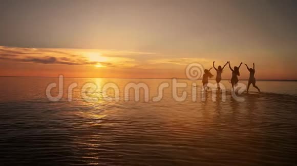 一群快乐的年轻人在美丽的夏日夕阳下在海滩上跳舞和喷洒视频的预览图