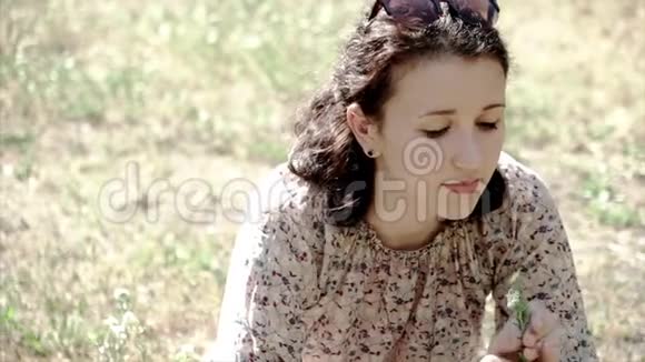 年轻美丽的黑发女孩肖像坐在草地上捧花视频的预览图