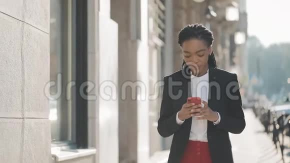 漂亮的女商人使用智能手机在商业中心附近的街道上行走黑色时尚可怕的家伙视频的预览图