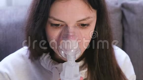 使用雾化器和吸入器进行治疗坐在沙发上的年轻女人通过吸入器面罩吸入特写视频的预览图