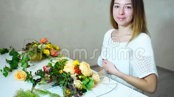 漂亮的女花装饰师看着镜头微笑着坐在桌子旁办公室里放着花束视频的预览图