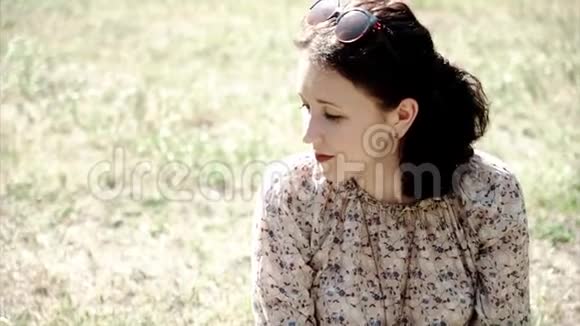 微笑的年轻女孩在镜头里看坐在草地上的肖像视频的预览图