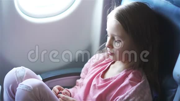 可爱的小女孩乘飞机旅行可爱的孩子在飞机窗口附近看电影慢动作视频的预览图