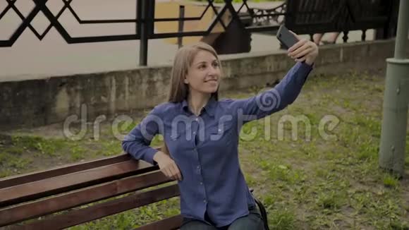 美丽的快乐女孩在公园的长凳上自拍视频的预览图