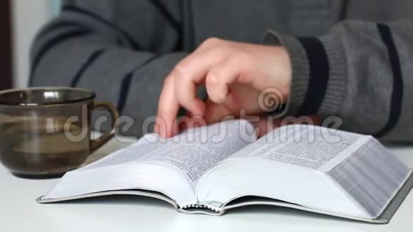 一个年轻人坐在桌子旁拿着一块银片读圣经翻过了几页视频的预览图