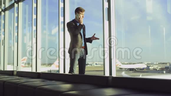 年轻的商人正在机场空无一人的候机大厅里谈论他的智能手机视频的预览图
