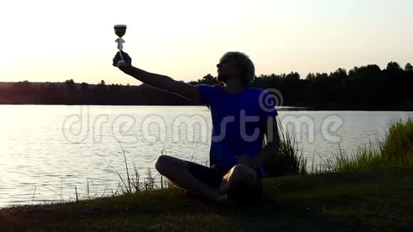 快乐的人坐着举起他的冠军碗在一个湖岸的斯洛莫视频的预览图