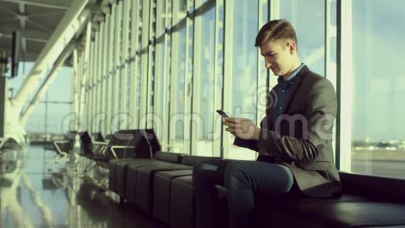 年轻的帅哥坐在机场的时候正在浏览一条短信视频的预览图
