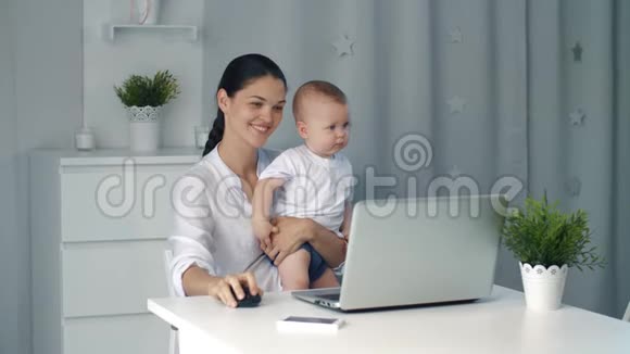 女商人母亲带着蹒跚学步的孩子在电脑前工作视频的预览图