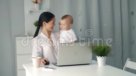 女妈妈带着蹒跚学步的孩子在电脑前工作视频的预览图