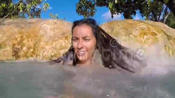 年轻女子在瀑布下微笑在翡翠池池塘与蓝色的水慢动作GoproSelfie高清泰国视频的预览图