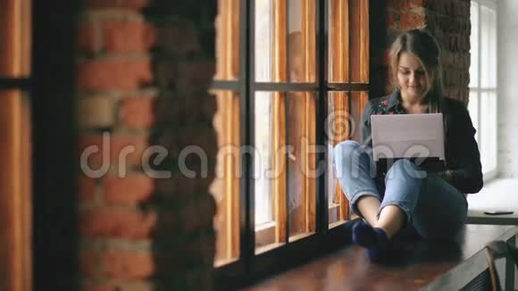 漂亮的年轻学生女孩手提电脑坐在室内大学教室的窗台上视频的预览图