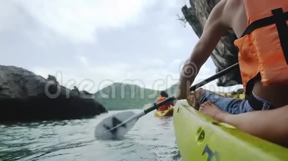穿着救生衣的健康强壮的男人穿着黄色皮艇在炎热的阳光下积极地驶近海边的悬崖视频的预览图