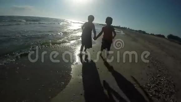 快乐的女孩和男孩赤脚在沙滩上奔跑视频的预览图