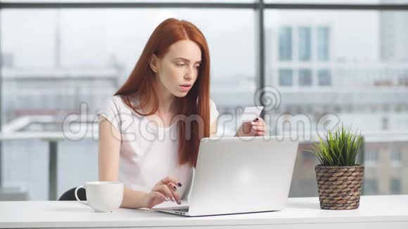 快乐红发女孩用信用卡和笔记本电脑在线购物视频的预览图