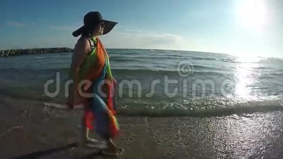 戴帽子的女人在日落时沿着海浪散步视频的预览图