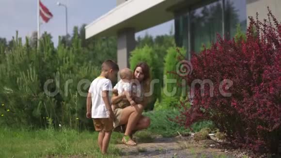 年轻的母亲在绿色的花园里和她的小儿子兄弟玩耍和玩耍家庭重视温暖的颜色夏天视频的预览图
