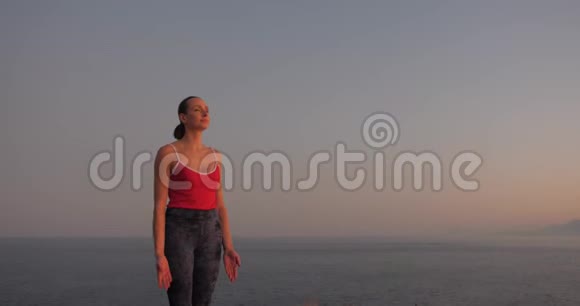 穿红色衣服的白人妇女在日落时在海边的悬崖上练习瑜伽放松身心视频的预览图