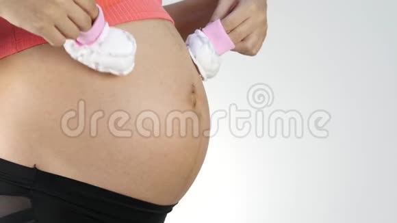 怀孕的妈妈穿着内衣在肚子上玩婴儿鞋4K视频的预览图