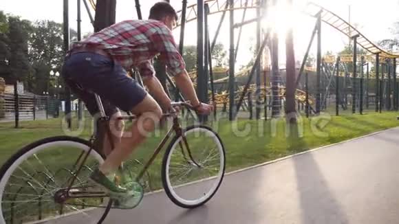 年轻的帅哥骑着一辆老式自行车在游乐园运动的家伙在户外骑自行车太阳照在背景上视频的预览图