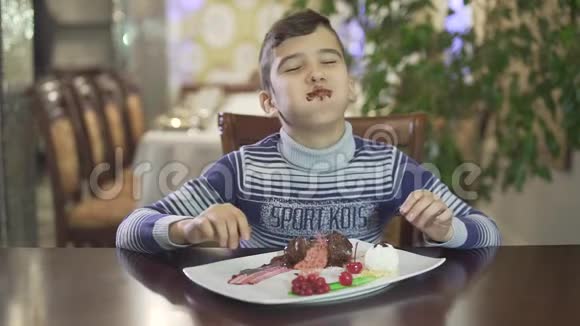 可爱的黑发小男孩喜欢吃巧克力甜点脏嘴手在高档餐厅舒适的氛围背景视频的预览图