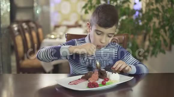 可爱的黑发小男孩喜欢吃巧克力甜点在高档餐厅舒适的氛围背景下凌乱的手嘴视频的预览图