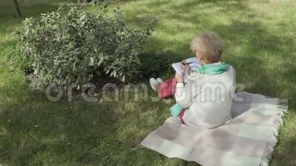 老妇人坐在草地上在笔记本上写字视频的预览图