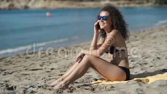 戴太阳镜的漂亮女孩在海滩上打电话视频的预览图