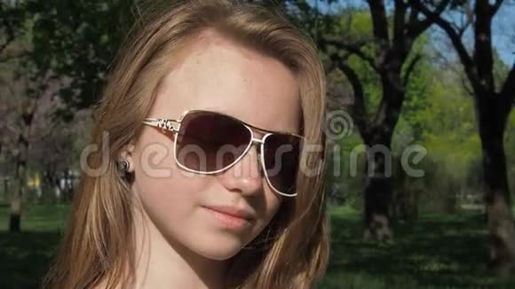 戴太阳镜的女孩特写一个长着雀斑的少女在大自然中摘下眼镜手拿手镯视频的预览图