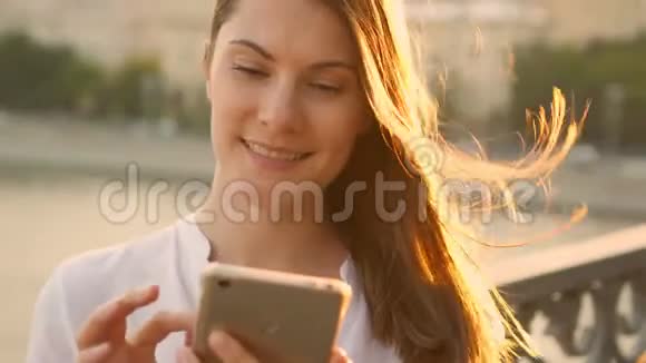 快乐的年轻女人在户外放松漂亮的女孩在她的智能手机上聊天夏日阳光灿烂视频的预览图