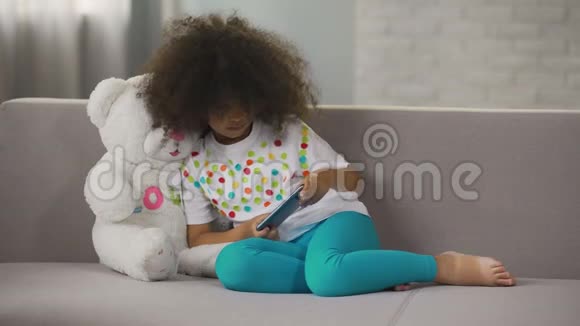 坐在沙发上玩手机游戏的美国小女孩视频的预览图