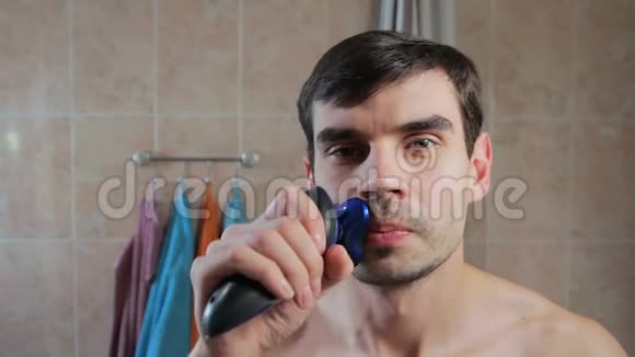 微笑的人用电动剃须刀在镜子前刮胡子伙计有刮胡子的乐趣视频的预览图