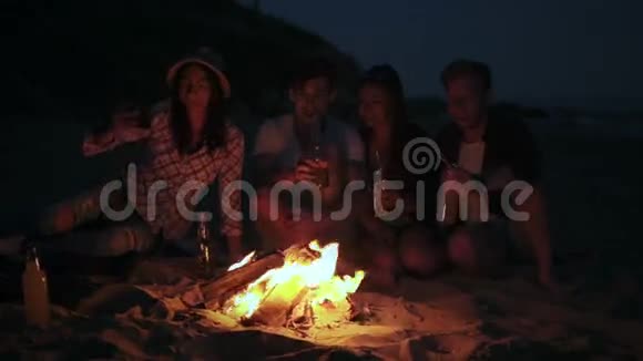 晚上在海滩上用篝火野餐年轻人快乐的朋友在电话里拍照视频的预览图