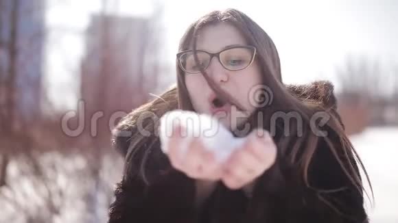 一个美丽可爱的女孩留着深色长发戴着眼镜走在冬天的公园里她微笑着玩雪很开心视频的预览图