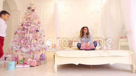 关爱的儿子在明亮的卧室里给母亲新年礼物盒里面有节日的树和礼物视频的预览图