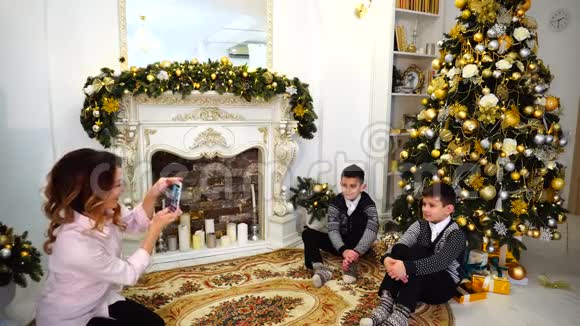 妈妈在智能手机上为儿子儿子的家庭相册拍照坐在客厅的地板上为节日装饰视频的预览图