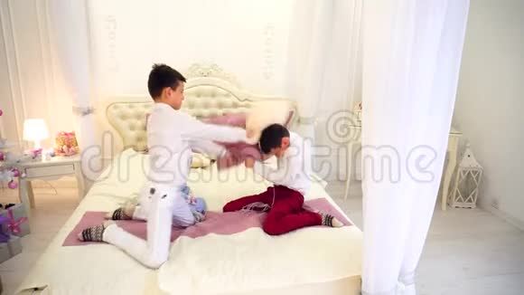 男孩们兄弟一起玩孩子们游戏在明亮的房间里用圣诞树在床上拍打枕头视频的预览图