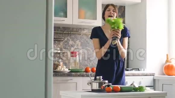 有趣的女人在厨房做饭时用生菜树枝跳舞唱歌视频的预览图