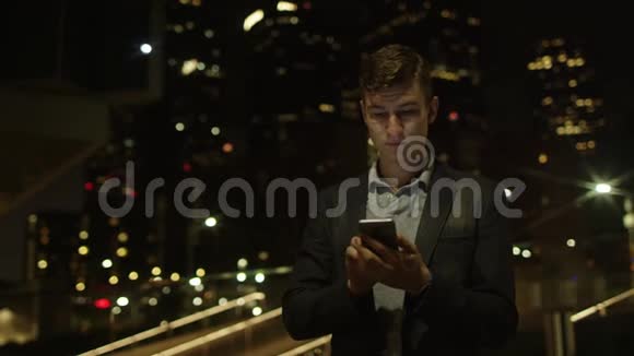 一个英俊的年轻学生站在街上用智能手机建立社交网络视频的预览图