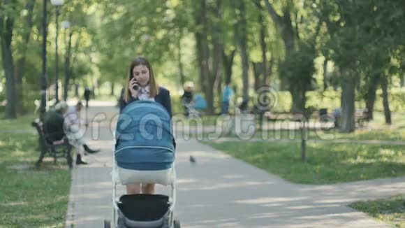 年轻的妈妈带着婴儿车在公园里散步然后打电话视频的预览图