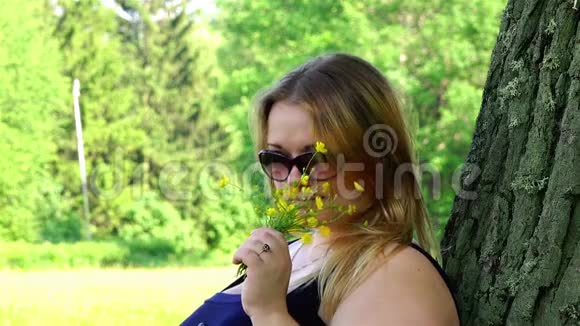 一个戴太阳镜的女孩在新鲜空气中吸入公园里野花的芬芳视频的预览图