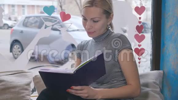 一个年轻的女人坐在窗边的咖啡馆里写着笔记本视频的预览图