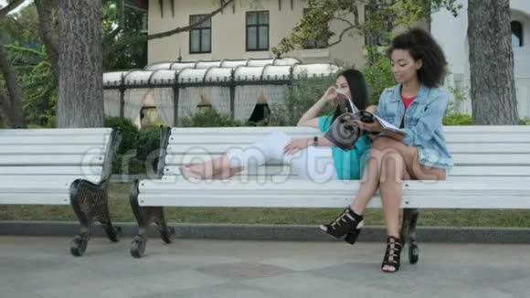 两个女孩坐在公园里聊天看杂志视频的预览图