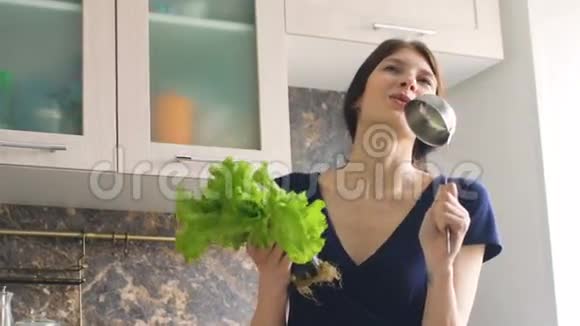 有趣的女人在厨房做饭的时候用大勺子和莴苣跳舞唱歌视频的预览图