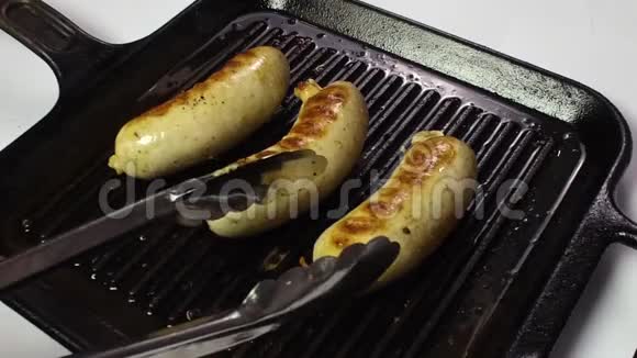 三根香肠在煎锅里煎厨师用钳子把它们钉在烤架上慢动作视频的预览图