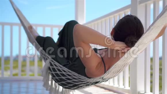 年轻女子在露台吊床上享受阳光明媚的一天的后景视频的预览图
