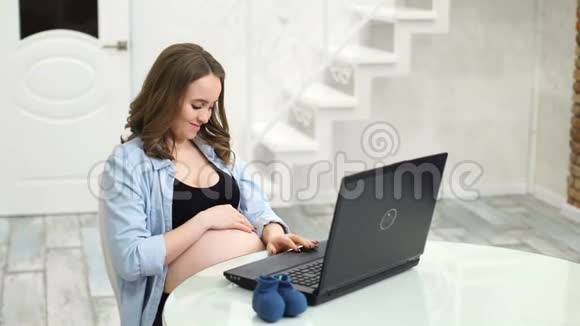 为宝宝网购一位坐在笔记本电脑旁的孕妇为自己的未来在网上商店挑选衣服视频的预览图