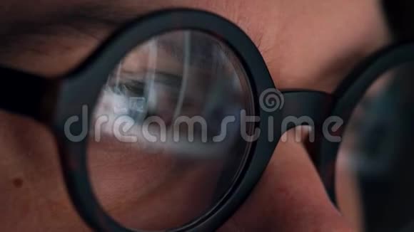 戴眼镜的人看着显示器和上网监视器屏幕反映在眼镜上视频的预览图