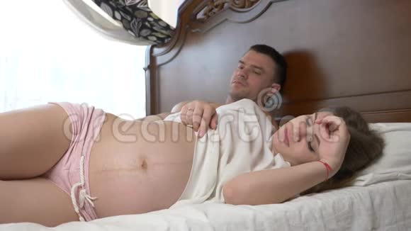 美丽的年轻孕妇抚摸着躺在床上的腹部4k慢动作视频的预览图
